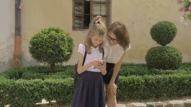 Frau-und-Kind-schauen-auf-Smartphone-zusammen,-Mutter-und-Tochter-Beziehung,-9-jährige-Schülerin-mit-einem-Outdoor-Handy-mit-Mutter