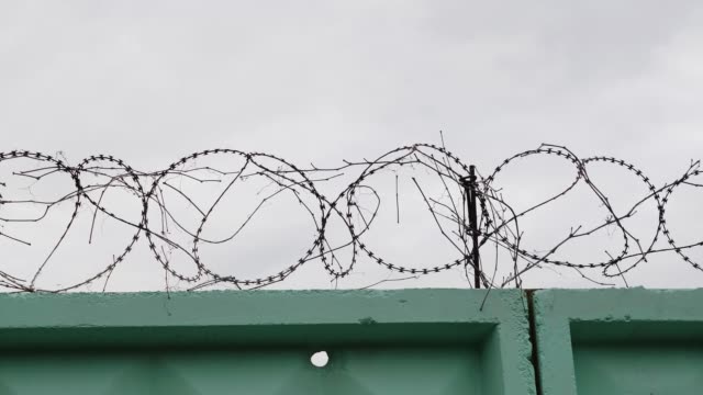 Prison-green-fence-with-barbed-wire.-Close-up-view-of-barbed-wire-in-jail.-Barbed-wire-fence