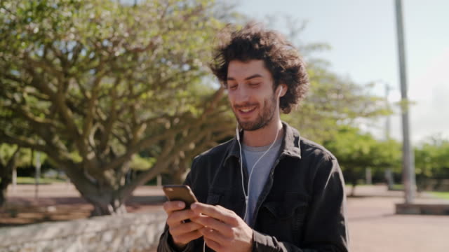 Portrait-of-a-happy-young-man-listening-to-music-on-mobile-phone-while-walking-in-the-park---a-happy-man-in-the-park