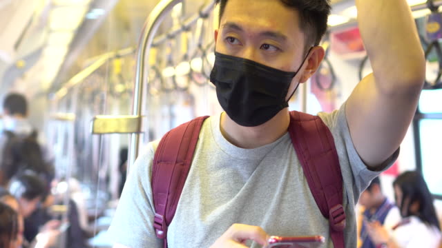 Close-up-of-one-young-Asian-man-wearing-a-black-surgical-face-mask-and-using-a-mobile-phone-in-subway-train-during-new-type-Coronavirus-Covid-19-pneumonia-outbreak-and-pm-2.5-smog-air-pollution-crisis-in-big-city
