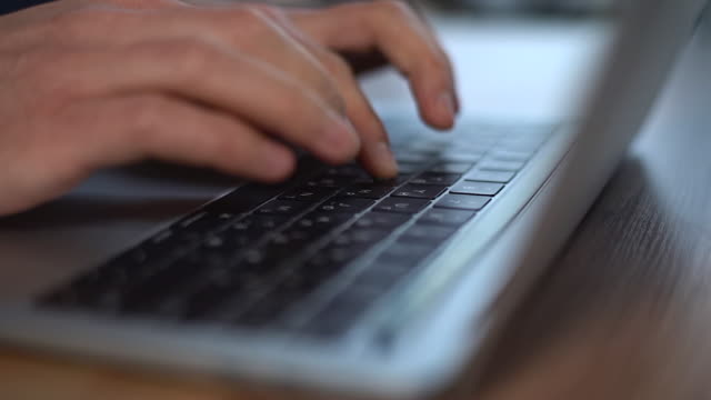 Primer-plano-de-las-manos-masculinas-escribiendo-en-el-teclado-del-ordenador-portátil,-moviendo-la-cámara