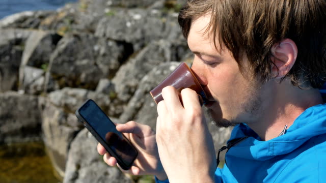 guy-drinks-coffee-from-cup-surfing-internet-with-phone