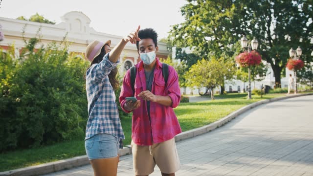 Afro-american-male-in-protective-mask-is-asking-female-the-right-route,-showing-map-on-cellphone