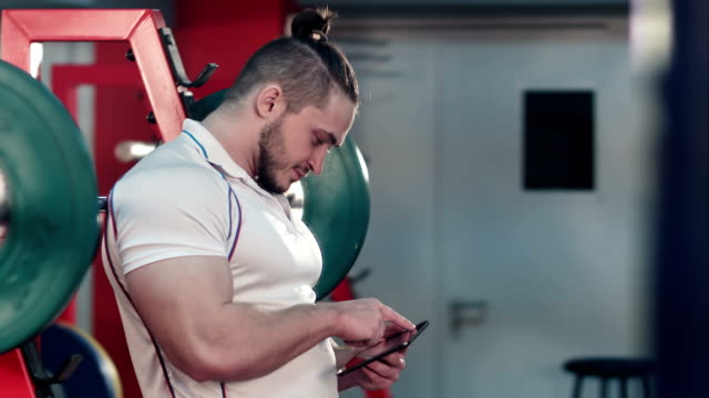 Bodybuilder-mit-digital-Tablette-zu-seinem-Training-im-Fitness-Studio-verfolgen