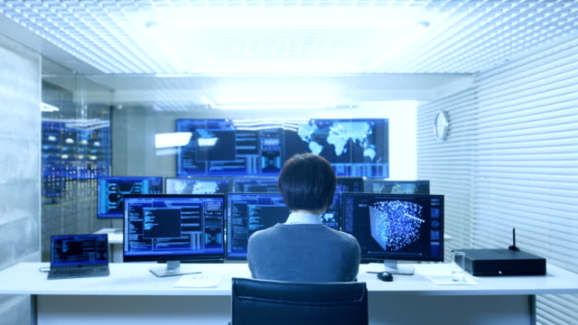 Back-View-of-the-IT-Engineer-Working-with-Multiple-Monitors-Showing-Graphics,-Functional-Neural-Network.-He-Works-in-a-Technologically-Advanced-System-Control-Data-Center.