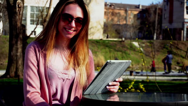 Reizendes-Mädchen-arbeiten-mit-Tablet-im-Park-und-ruht-in-Sonnenbrille