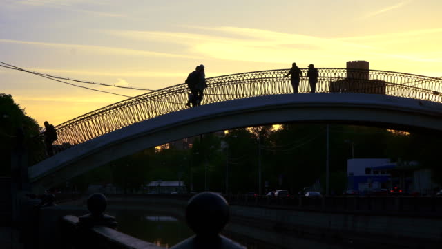 Silhouetten-von-Menschen,-die-Überquerung-des-Kanals-auf-eine-Bucklige-Brücke