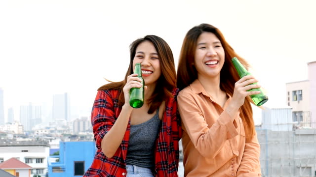 Junge-asiatische-Frau-lesbisches-Paar-klirrende-Flaschen-Bier-party-am-Dach.