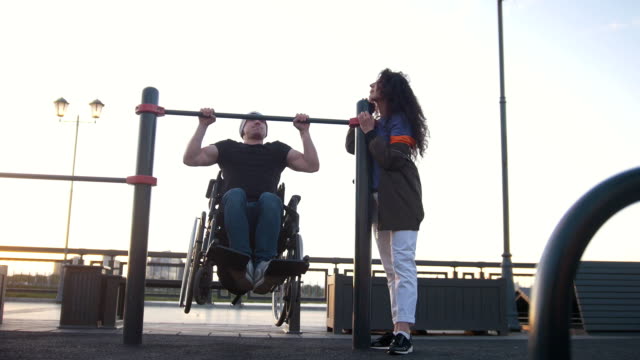 Hombre-discapacitado-en-silla-de-ruedas-tirado-para-arriba-en-la-barra-junto-a-la-joven-al-aire-libre