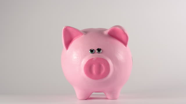 Zeitraffer:-Männliche-Hand-wirft-Münzen-in-ein-rosa-Schweinchen-sparschweinchen