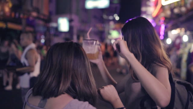 Slow-Motion---Reisende-Backpacker-asiatische-Frauen-Lesben-LGBT-Paare-tanzen-zusammen.-Weibliche-Alkohol-oder-Bier-mit-Freunden-trinken-und-feiern-auf-der-Khao-San-Road-in-Bangkok,-Thailand.