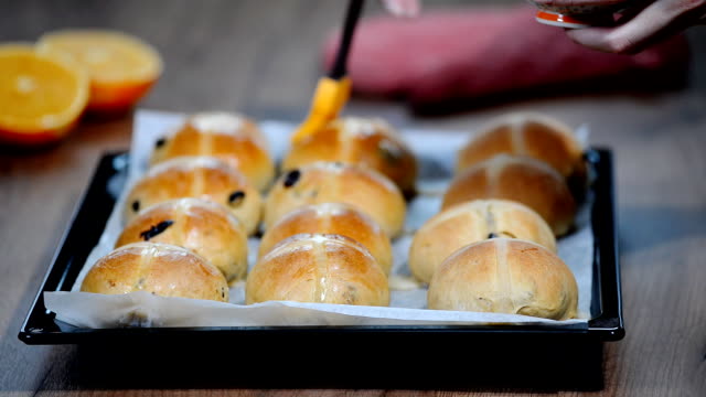 Hot-cross-buns-on-baking-tray.-Female-hands-cover-with-syrup.