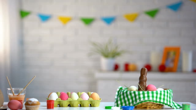 Cute-girl-jumping-like-rabbit-from-under-table-and-looking-at-bright-Easter-eggs