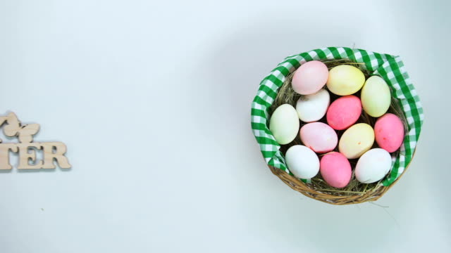 Mano-de-mujer-poniendo-feliz-Pascua-decoración-cerca-de-canasta-pintado-huevos,-vacaciones