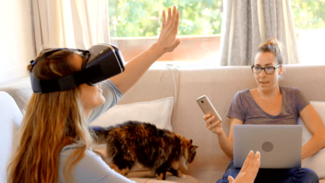 Lesbisches-Paar-mit-virtual-Reality-Kopfhörer-und-Laptop-im-Wohnzimmer-4k