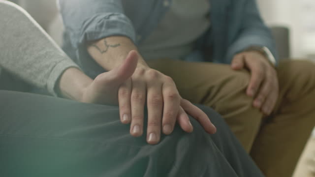 Close-Up-of-Two-Male-Hands-Gently-Touching-and-Holding-Each-Other.-Cute-Queer-Relationship-Concept.-Gay-Couple-are-Casually-Dressed.-Room-is-Bright-and-Sunny.