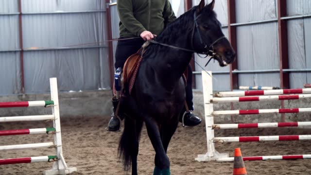 in-special-hangar,-a-young-disabled-man-learns-to-ride-a-black,-thoroughbred-horse,-hippotherapy.-man-has-an-artificial-limb-instead-of-his-right-leg.-concept-of-rehabilitation-of-disabled-with-animals