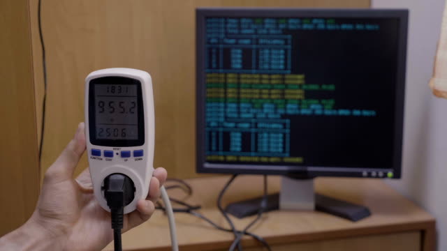 Wattmeter-indicating-power-usage-rate-of-cryptocurrency-mining-rig-and-pc-with-cryptic-process-running-on-display