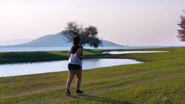 Eine-fette-asiatische-Frau,-die-abends-im-natürlichen-Sonnenlicht-joggt.
Sie-versucht,-mit-Übung-Gewicht-zu-verlieren.--Konzept-Gesundheit-mit-Bewegung.