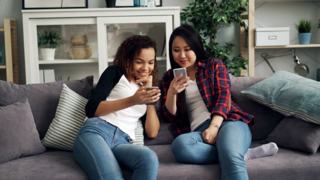 Lächelnde-junge-Frauen-nutzen-Smartphones,-die-reden-und-lachen,-wenn-sie-auf-dem-Bildschirm-sitzen-und-soziale-Medien-und-moderne-Technologien-genießen.-Kommunikation-und-Jugendkonzept.