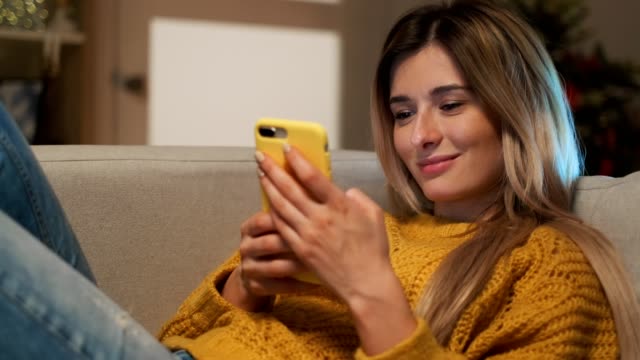 Attraktive-blonde-Schülerin-Texting-auf-ihrem-Telefon.-Frau-mit-Smartphone,-um-mit-Freunden-in-sozialen-Netzwerken-tippen-Nachrichten-zu-kommunizieren-und-durch-das-Internet-sitzen-auf-Komfort-Sofa-zu-Hause