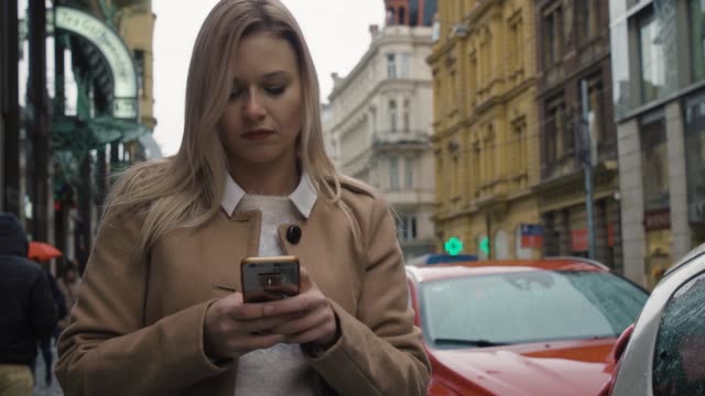 Eine-junge-schöne-Frau-arbeitet-an-einem-Herbsttag-auf-einem-Smartphone-in-einer-Straße