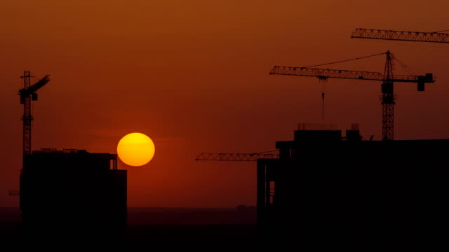 The-building-with-cranes-on-the-sunrise-background.-time-lapse