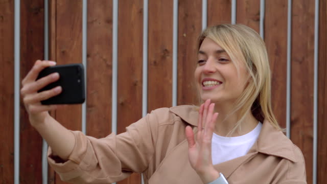 Blonde-Frau-spricht-per-Videoanruf-auf-ihrem-Smartphone-im-Freien