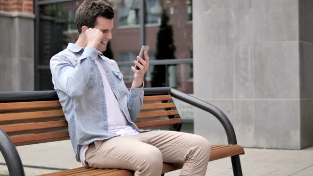 Al-aire-libre-hombre-joven-emocionado-por-el-éxito-en-smartphone