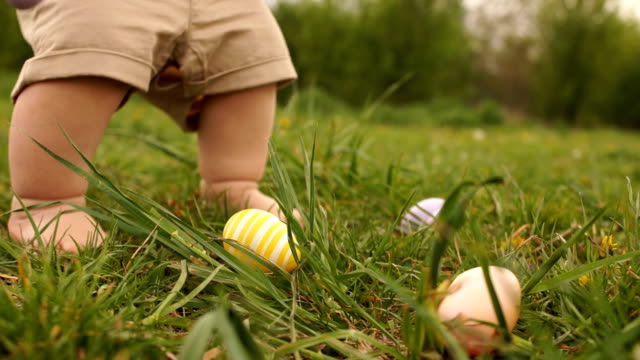 Cerca-de-las-piernas-de-bebé.-Un-niño-está-buscando-huevos-de-Pascua-en-la-hierba.-Feliz-familia-de-Pascua