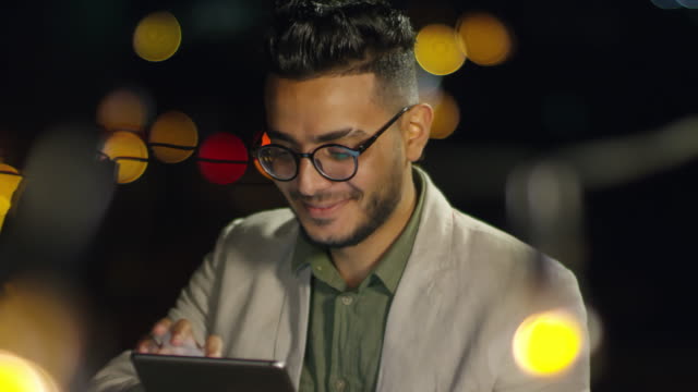 Lächelnd-Arab-Man-spielt-auf-digitales-Tablet-auf-dem-Dach-in-der-Nacht