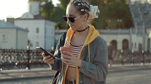 Mujer-joven-en-jeans-caminando-por-la-ciudad,-mensajería-de-texto-usando-el-teléfono-móvil