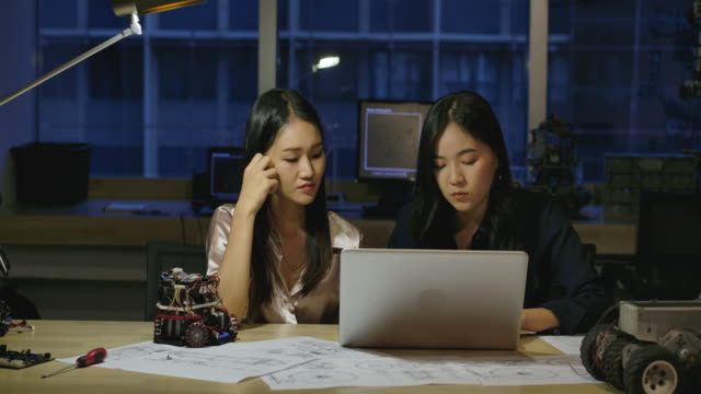 Mujeres-Ingenieros-de-Electrónica-Examinando-Proyecto-en-la-Oficina.-Dos-mujeres-asiáticas-comparan-datos-en-un-ordenador-personal.-Personas-con-concepto-de-tecnología-o-innovación.