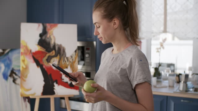 Malerin,-die-Apple-isst-und-Smartphone-benutzt