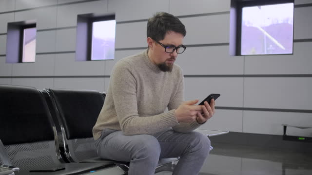 Man-is-looking-on-display-of-mobile-phone-sitting-on-chair
