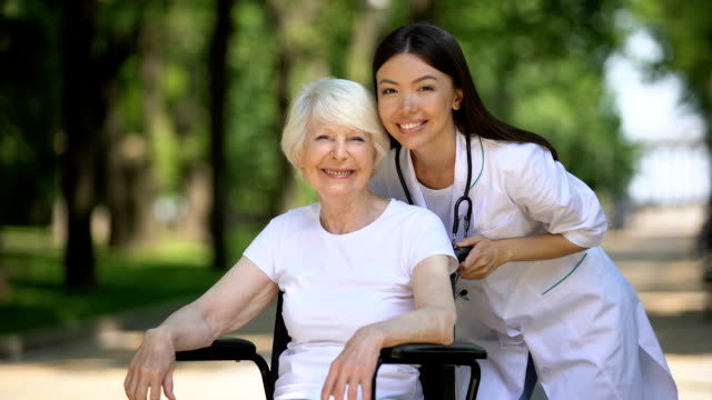 Nurse-and-old-handicapped-woman-smiling-at-camera-and-showing-thumbs-up-gesture