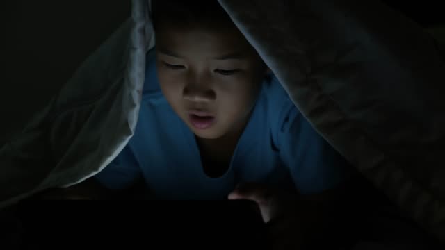Niño-pequeño-usando-tableta-bajo-la-manta-por-la-noche-en-la-cama.