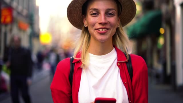 Close-up-portrait-of-authentic-Caucasian-female-standing-with-smartphone-in-hands-and-sincerely-laughing-on-camera