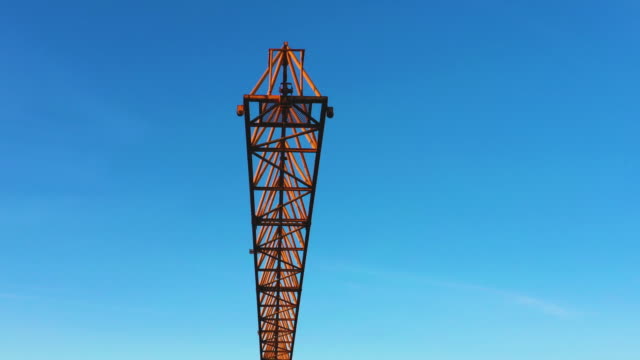 A-construction-crane-swaying-slightly-in-the-wind-against-the-morning-sky.-Close-up,-aerial-video