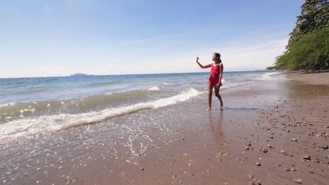 Vlogger-viaje-femenino-en-un-vestido-rojo-filmando-vlog-en-la-orilla-del-mar.