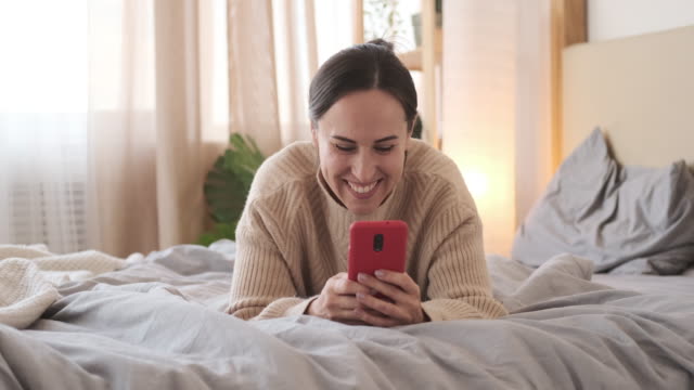 Mujer-teniendo-mensajes-de-texto-divertidos-en-el-teléfono-móvil-en-la-cama