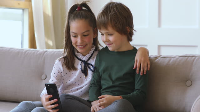 Two-kids-boy-girl-learning-using-smartphone-together-on-sofa