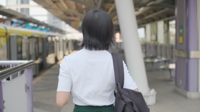 Portrait-of-asian-woman-with-earphone-listening-music-and-using-smartphone-for-chatting-with-friends-or-browsing-while-waiting-for-a-train.-Technology-in-everyday-life-and-travel.