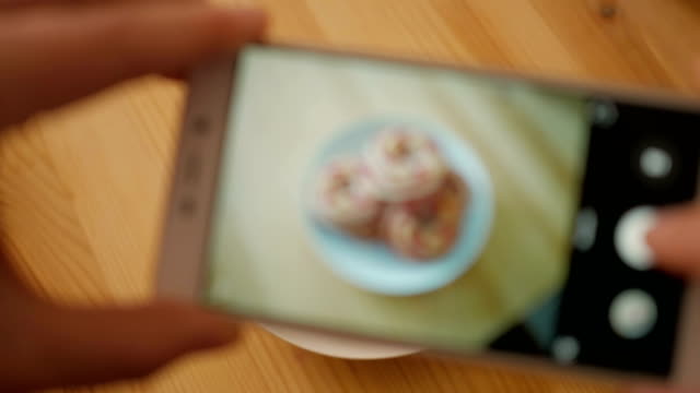 Closeup-of-man-hand-making-photo-of-sweet-dessert-on-mobile-phone.--Male-photographs-on-the-smartphone-a-round-soft-biscuit-on-a-wooden-table-close-up.
