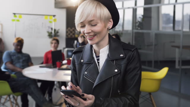 Attraktive-Geschäftsfrau-arbeitet-am-Smartphone-mit-Gruppe-junger-Geschäftsleute-im-Hintergrund