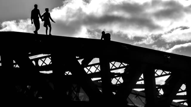 Silhouetten-von-jungen-Menschen-flanieren-und-die-Bilder-von-einander-in-einer-prekären-Situation-auf-der-Oberseite-der-Brücke,-Zeitraffer
