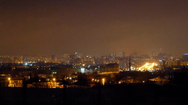 Winter-Nacht-Stadtbild-mit-dem-Licht-der-Straßenlampen-in-der-Nähe-der-Straßen.-Autos-fahren-auf-nasser-Fahrbahn