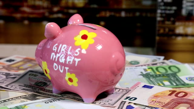 Pink-piggy-bank-on-rotating-surface-with-dollars-and-euro-banknotes.