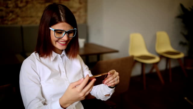 Glückliche-junge-Frau-sitzt-im-Café-SMS-auf-ihrem-Smartphone