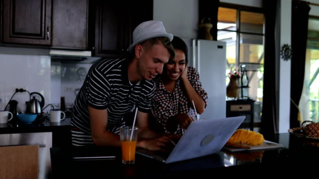 Einige-verwenden-Laptop-Computer-umarmen,-glückliche-junge-Frau-und-Mann-im-Küchenstudio-sprechen-moderne-Haus-innen